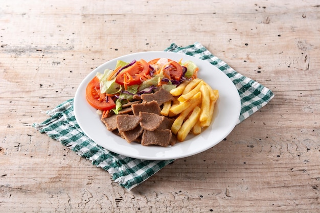 Plato de kebab, verduras y patatas fritas en mesa de madera