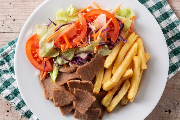 Plato de kebab, verduras y patatas fritas en mesa de madera