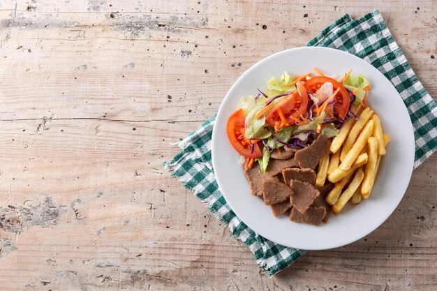 Plato de kebab, verduras y patatas fritas en mesa de madera