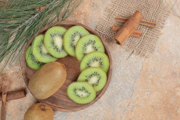 Plato de kiwi fresco y palitos de canela sobre fondo de mármol.