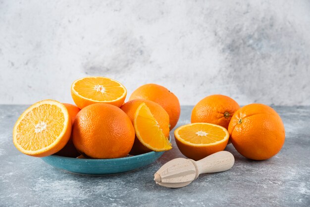 Un plato lleno de frutas naranjas jugosas en rodajas y enteras con escariador de madera.