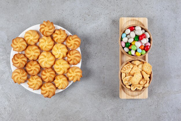 Un plato lleno de galletas caseras con dos tazones de galletas y dulces en una bandeja sobre fondo de mármol. Foto de alta calidad