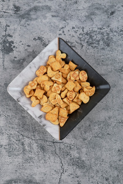 Plato lleno de galletas saladas secas sobre fondo de mármol.