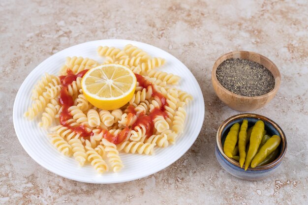 Plato de macarrones con pequeños cuencos de pimienta negra y pimientos en escabeche sobre superficie de mármol