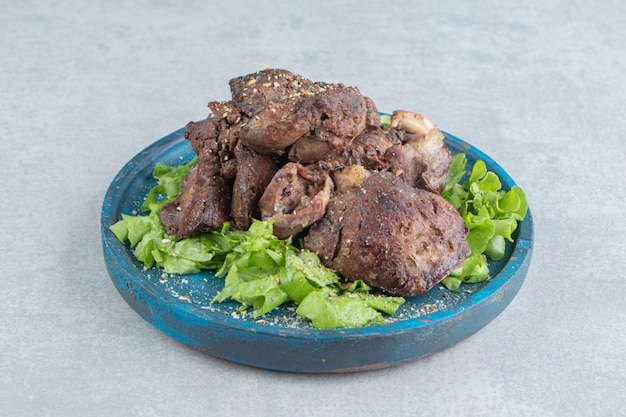 Un plato de madera azul de carne frita y lechuga en rodajas.