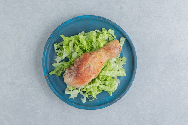 Un plato de madera de carne de pierna de pollo frito con lechuga en rodajas.