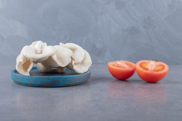 Un plato de madera con champiñones y tomate en rodajas.