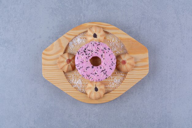 Un plato de madera de delicioso donut rosa con galleta dulce.