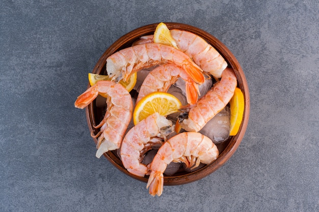 Un plato de madera de deliciosos camarones con cubitos de hielo y rodajas de limón sobre una superficie de piedra