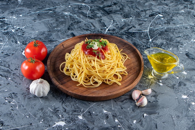 Plato de madera de deliciosos espaguetis con salsa de tomate y verduras en la superficie de mármol.