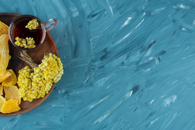 Plato de madera de frutos secos y vaso de té sobre fondo azul.