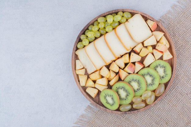 Un plato de madera lleno de frutas en rodajas y pan. Foto de alta calidad