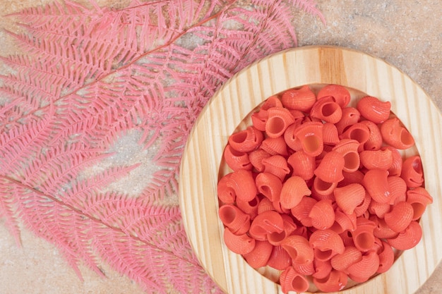 Un plato de madera lleno de macarrones rojos sin preparar.