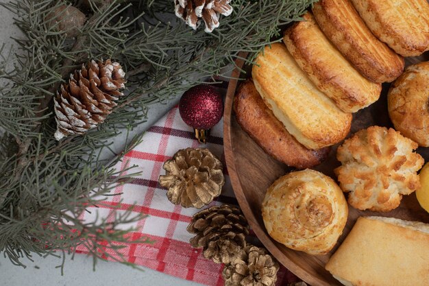 Un plato de madera lleno de pasteles dulces con bolas de Navidad y piñas.