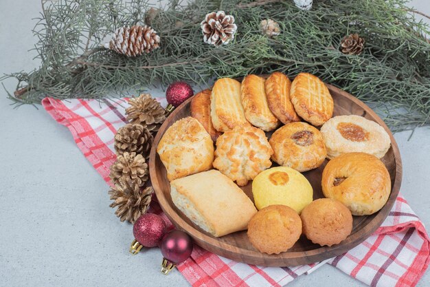 Un plato de madera lleno de pasteles dulces con bolas de Navidad y piñas.