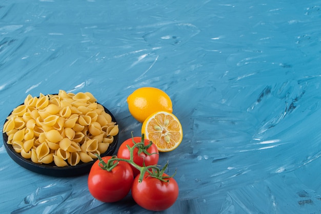 Un plato de madera negra de pasta cruda con limón y tomates rojos frescos.