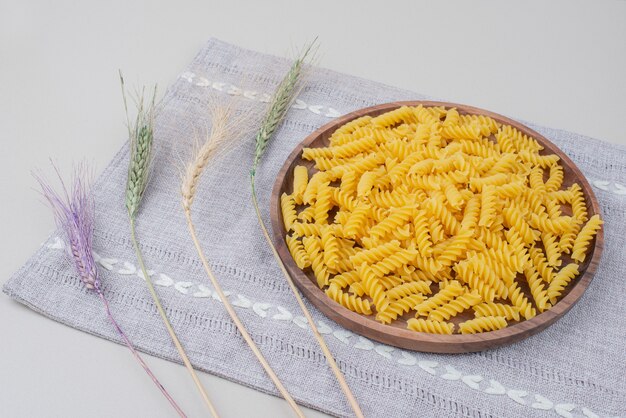 Plato de madera de pasta cruda sobre mantel con trigo colorido.