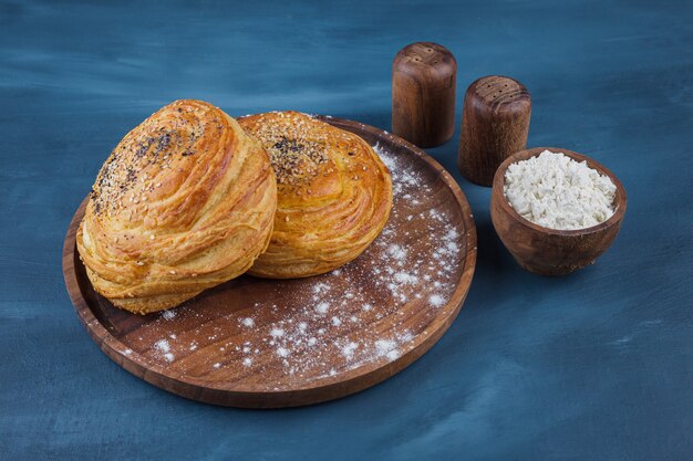 Plato de madera de pasteles dulces con semillas sobre superficie azul.