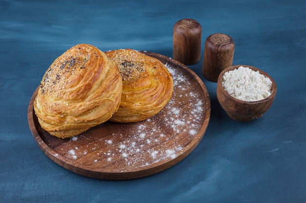 Plato de madera de pasteles dulces con semillas sobre superficie azul.