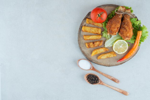 Un plato de madera de pollo frito y patatas.