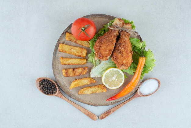 Un plato de madera con pollo frito y verduras sobre una mesa de mármol.