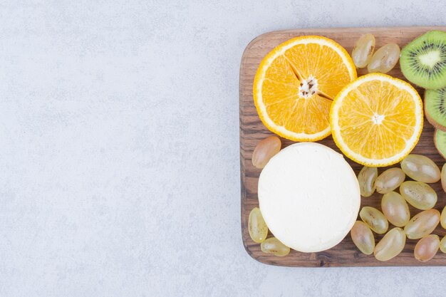 Un plato de madera con queso en rodajas y frutas. Foto de alta calidad