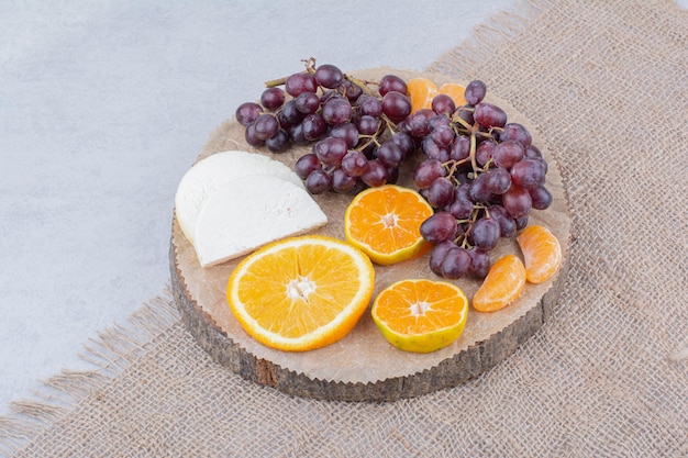 Un plato de madera con queso en rodajas y frutas. Foto de alta calidad