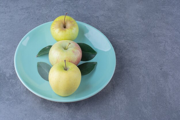 Un plato de manzanas maduras y hojas sobre la mesa de mármol.