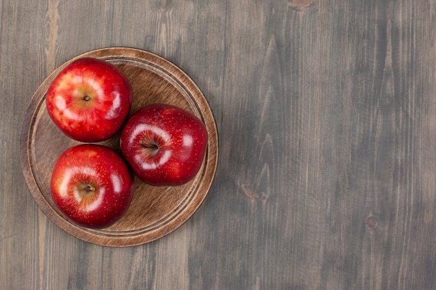 Un plato marrón con jugosas manzanas rojas sobre una mesa de madera. Foto de alta calidad