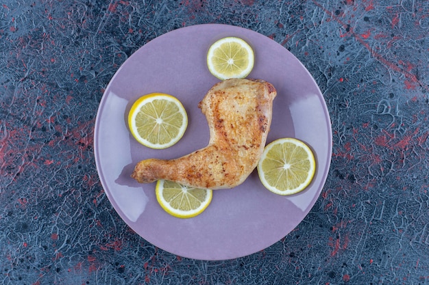 Un plato morado con carne de pierna de pollo con rodajas de limón.