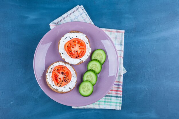 Un plato morado de pepino en rodajas y sándwiches con queso y tomate en rodajas.