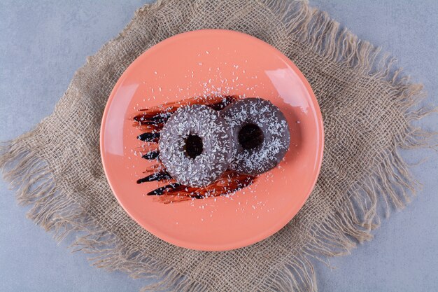 Un plato naranja de deliciosas donas de chocolate con chispitas sobre una tela de saco