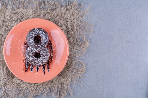 Un plato naranja de deliciosas donas de chocolate con chispitas sobre una tela de saco