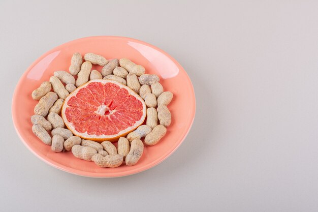 Plato naranja de rodaja de pomelo y maní orgánico sobre fondo blanco. Foto de alta calidad