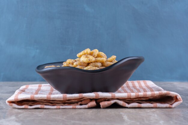 Un plato negro de anillos de cereales saludables para el desayuno sobre un mantel.