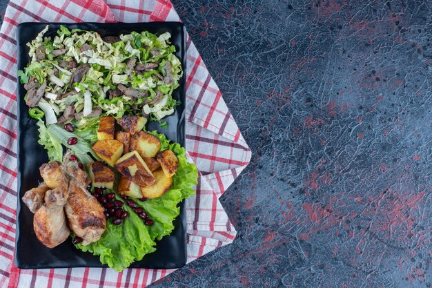 Un plato negro de carne de pollo con ensalada de verduras.