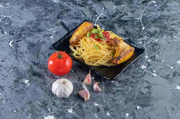 Plato negro de fideos con alitas de pollo frito sobre superficie de mármol.