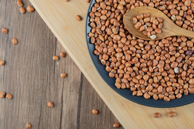 Un plato negro lleno de frijoles rojos crudos secos con cuchara de madera.