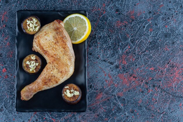 Un plato negro de muslo de pollo a la plancha con berenjena frita.