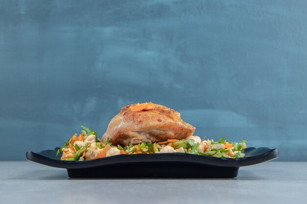 Un plato negro de pollo frito, carne y ensalada de verduras.