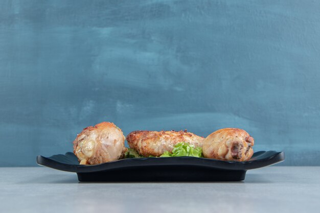 Un plato negro de pollo frito, carne y ensalada de verduras.