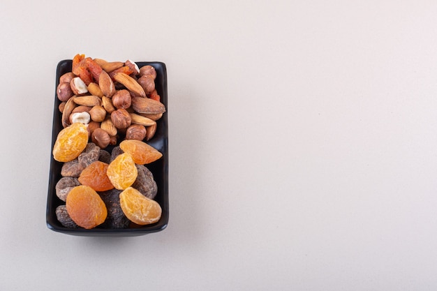 Plato oscuro de diversos frutos secos orgánicos sobre fondo blanco. Foto de alta calidad