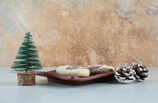 Foto gratuita un plato oscuro de dos deliciosas galletas con piñas y árbol de navidad.