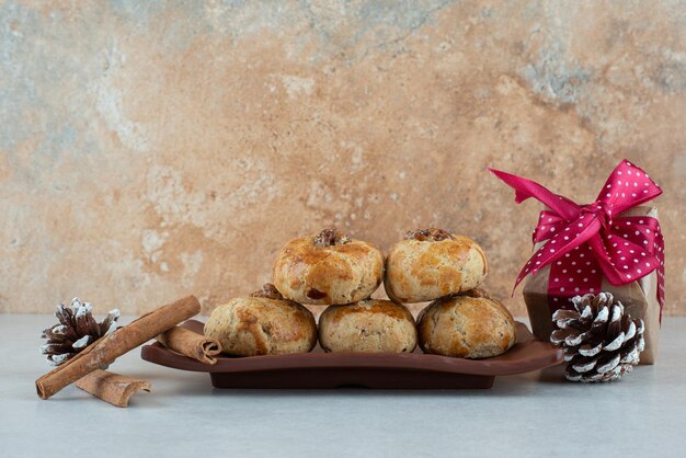 Un plato oscuro de galletas con un pequeño regalo de Navidad y piñas.