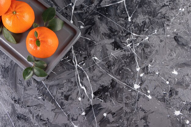 Plato oscuro de jugosas naranjas enteras sobre superficie de mármol