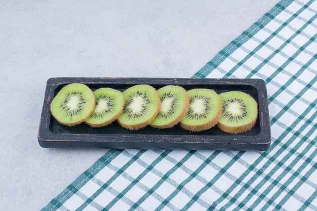 Un plato oscuro de kiwi fresco en rodajas sobre un mantel. Foto de alta calidad