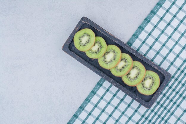 Un plato oscuro de kiwi fresco en rodajas sobre un mantel. Foto de alta calidad