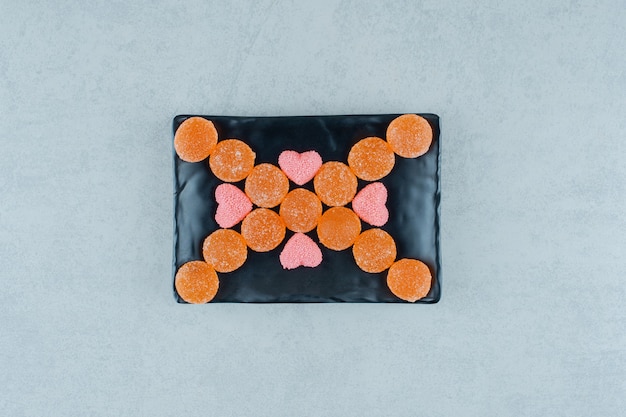 Un plato oscuro lleno de caramelos de gelatina de naranja dulce con dulces de gelatina en forma de corazón rosa