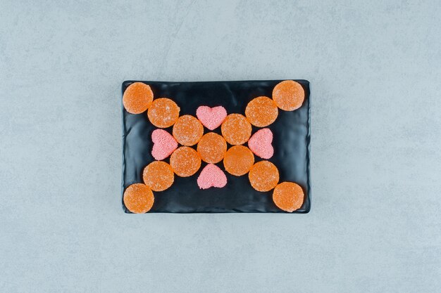 Un plato oscuro lleno de caramelos de gelatina de naranja dulce con dulces de gelatina en forma de corazón rosa