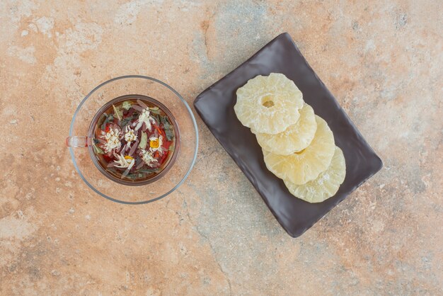 Un plato oscuro lleno de piña saludable seca y una taza de té